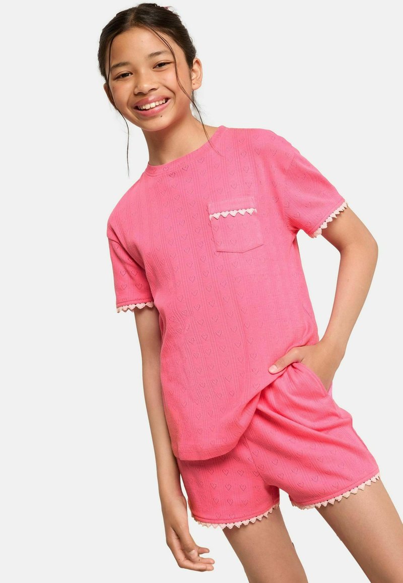 Completo in cotone rosa composto da top a maniche corte con tasca sul petto e bordi scallop, abbinato a pantaloni corti coordinati.
