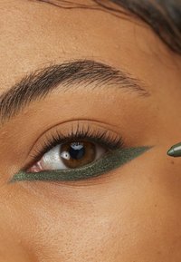 Grønn eyeliner påført øyelokket, som kontrasterer med en naturlig hudtone; brune øyne viser definerte vipper og subtilt bryn.