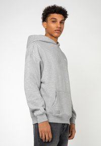 Grijze hoodie met een frontzak, geribde manchetten en een logodetail op de borst, gemaakt van een zachte, gestructureerde stof.