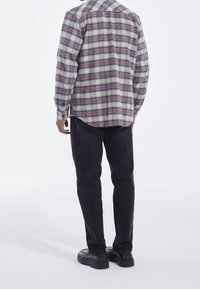 Geruite shirt in blauw, rood en crème. Lange mouwen, knoopsluiting van kraag en gebogen zoom. Zwarte slim-fit broek en zwarte schoenen.