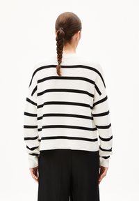 Weißer Pullover mit schwarzen horizontalen Streifen, locker sitzend, mit gesenkten Schultern und gerippten Bündchen. Rückansicht, getragen mit schwarzen Hosen.