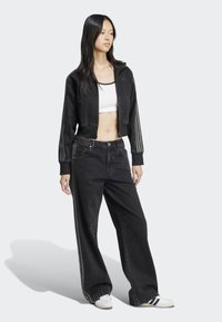 Schwarze kurze Jacke mit drei Streifen an den Ärmeln, kombiniert mit weiten schwarzen Jeans und weißen Turnschuhen. Einfaches, lässiges Design.