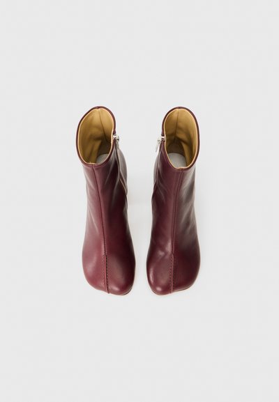 Bottines en cuir bordeaux avec une texture lisse, un léger brillant et des fermetures éclair sur les côtés, présentant un design minimaliste et un bout arrondi.