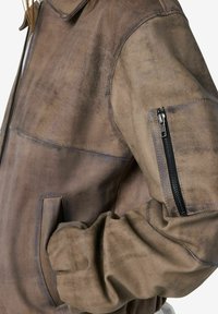 Veste en cuir marron vieilli avec poche zippée sur la manche supérieure et main insérée dans la poche latérale.