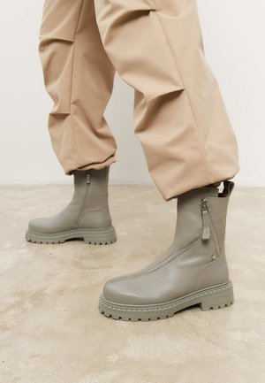 Grå læder ankelstøvler med lomme lynlås, kraftig sål og teksturerede detaljer. Kombination med beige, løstsiddende bukser.
