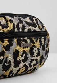 Borsa cosmetica di forma rotonda con stampa leopardata in nero, oro e argento, dotata di una zip nera prominente e di un'etichetta metallica "DAY ET".