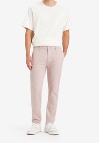 Ljusbeige kortärmad t-shirt i kombination med ljusrosa slim-fit byxor och vita sneakers. Enkel design och mjuk textur.