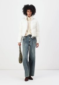 Giacca puffer bianca, dolcevita crema, jeans a gamba larga blu, stivaletti marroni, borsa verde. Materiale morbido, design casual, vestibilità ampia.