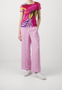 Lyhythihainen, istuva t-paita kirkkaan vaaleanpunaisena, jossa on monivärisiä lehtikuvioita; yhdistettyinä vaaleanpunaisiin, leveisiin pellavahousuihin ja valkoisiin kenkiin.