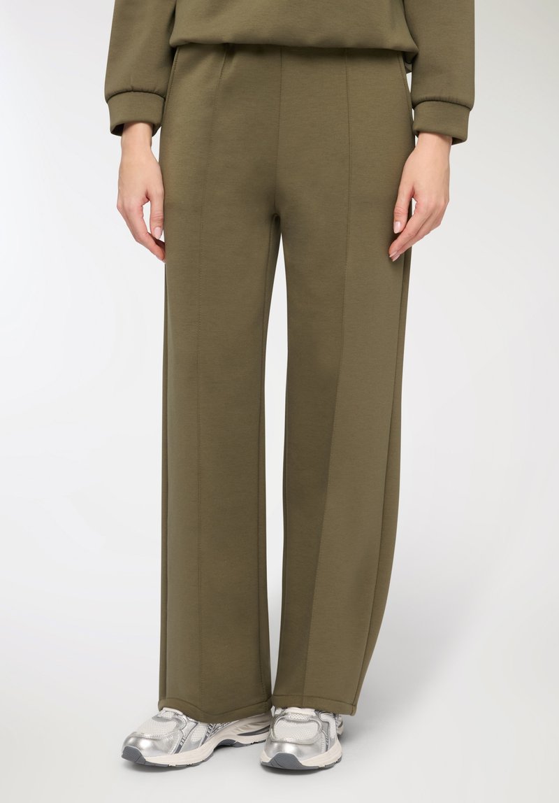 Pantaloni a gamba larga di colore verde oliva realizzati in tessuto morbido con dettagli cuciti, abbinati a scarpe sportive argento. Vita elastica per il massimo comfort.