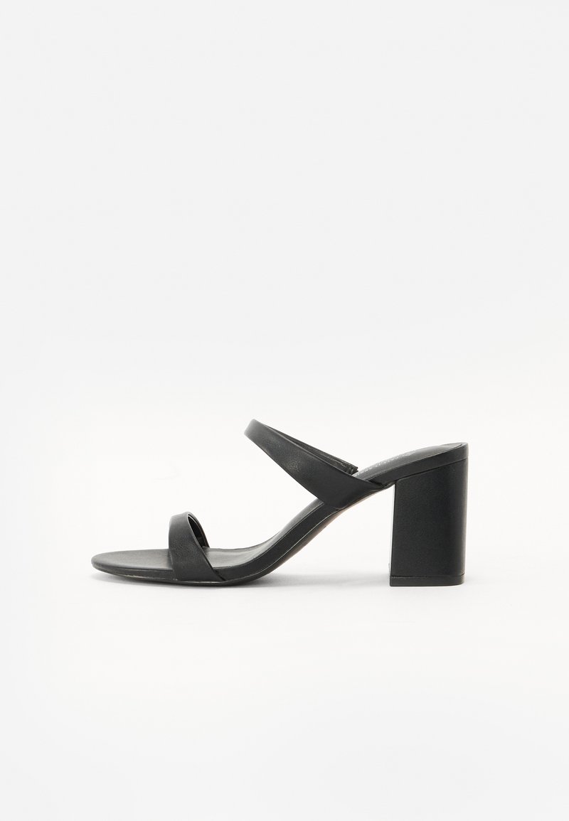 Sandale noire à talons hauts avec deux sangles épurées, un large talon carré et une finition mate lisse, conçue pour le confort et la stabilité.
