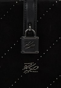 Czarna zamszowa torebka na ramię z gładkim skórzanym paskiem. Posiada metalowe akcenty, zapięcie na kłódkę oraz dekoracyjne cyrkonie w rozproszonym wzorze.