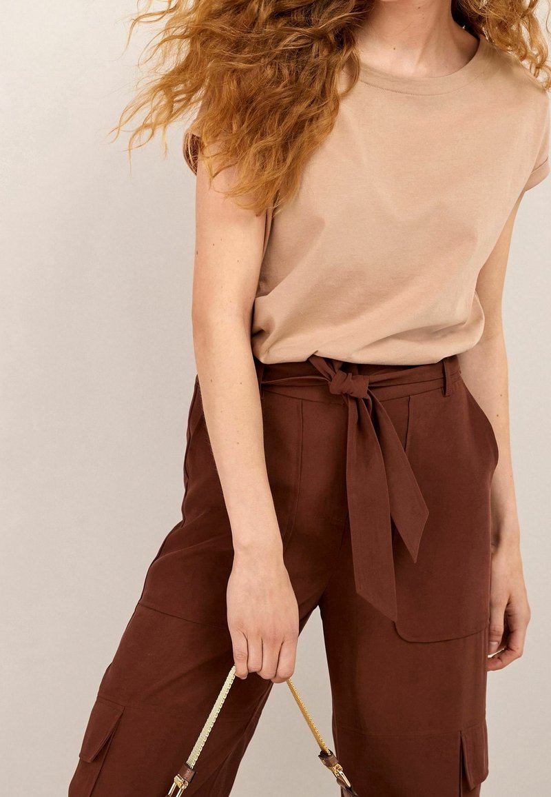 Beige short-sleeve top paired with high-waisted, brown, belted cargo pants featuring side pockets and smooth fabric texture.