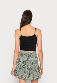 Top cropped preto com alças finas, combinado com uma saia verde em forma de sino com um padrão de pontos pretos. Texturas suaves e design ajustado.