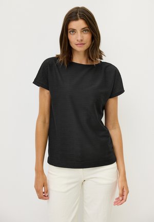 Haut noir à manches courtes avec une surface texturée et un décolleté large. Assorti à un pantalon ajusté de couleur claire pour le contraste.