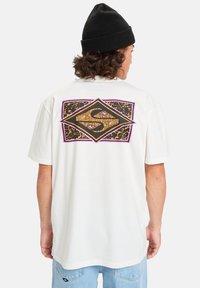 Camiseta de algodón blanca con mangas cortas y un gráfico en la parte posterior que presenta una forma de diamante en letras negras, rosas y doradas.