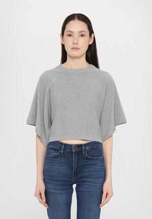 Maglione corto grigio con maniche corte e ampie. Tessuto a maglia morbido e scollatura rotonda, abbinato a jeans skinny blu scuro.