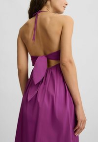 Purple halter dress with a tied back, featuring a fitted bodice and a flowing skirt. Smooth fabric with a soft sheen and a bow accent.