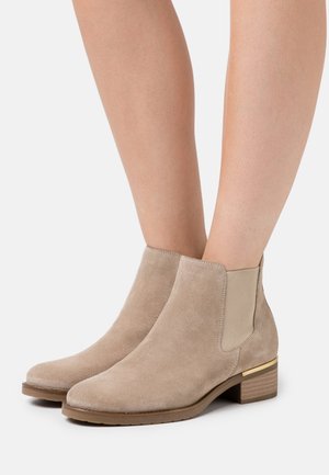Beige suede ankle boots with elastic side panels, square toe, and a low stacked heel featuring a gold accent detail.