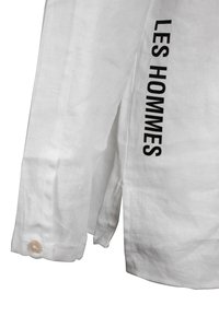 Witte linnen blouse met lange mouwen, knoopmanchet en "LES HOMMES" in vet zwart gedrukt langs de zijkant. Glad, lichtgewicht stof.
