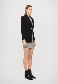 Blazer nero su misura con un singolo bottone argento, abbinato a un mini abito a righe bianche e nere e stivaletti neri alla caviglia. Texture liscia.