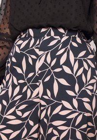 High-waisted trousers in navy with a light pink leaf pattern. Smooth fabric with a fitted waistband, featuring vertical pleats for structure.