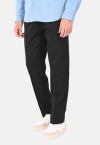 Pantaloni neri a taglio dritto, realizzati in un materiale morbido, con dettagli di cucitura discreti. Abbinati a sneakers bianche e beige.