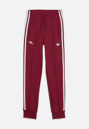 Pantalones de chándal burdeos con franjas laterales blancas, que cuentan con bolsillos delanteros con cremallera y logotipos bordados, fabricados en un tejido suave y elástico.