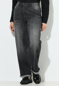 Zwarte spijkerbroek van denim met een vervaagde grijze was, rechte pijpen en versierd met rhinestones langs de voorzakken. Opgerolde boorden.