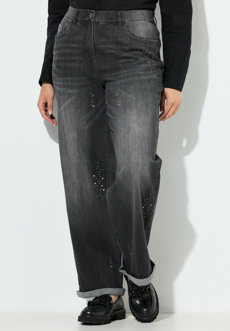 Zwarte spijkerbroek van denim met een vervaagde grijze was, rechte pijpen en versierd met rhinestones langs de voorzakken. Opgerolde boorden.