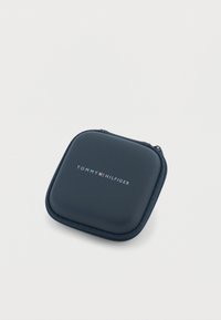 Tamsiai mėlynas dėklas su užtrauktuku ir lygiu paviršiumi, ant kurio yra baltos ir raudonos spalvų logotipas „TOMMY HILFIGER“. Kvadratinės formos, kompaktiško dydžio.