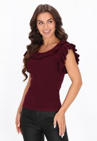 Top bordeaux cu textură ribbed, având mâneci scurte volănașe și un decolteu larg. Asortat cu pantaloni negri mulați.