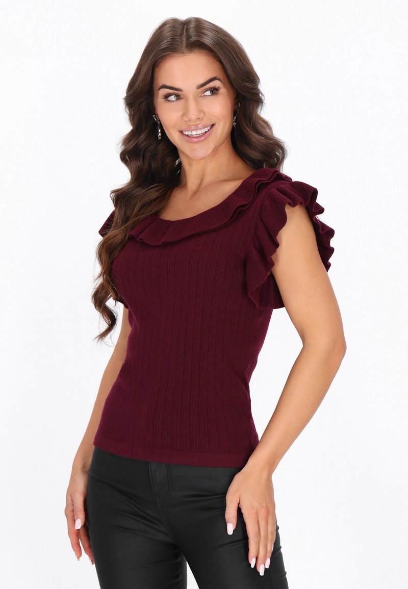 Top bordeaux cu textură ribbed, având mâneci scurte volănașe și un decolteu larg. Asortat cu pantaloni negri mulați.