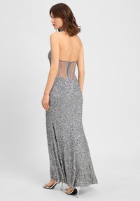 Silberne Paillettenkleid mit tailliertem Oberteil und Netzrückenverzierung. Verfügt über einen bodenlangen Rock und Riemchen-High Heels.