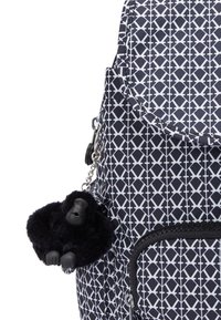 Mochila navy con patrón geométrico blanco, que presenta un llavero de gorila negro peludo sujeto por una cadena plateada y un bolsillo frontal con cremallera.