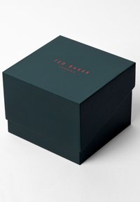 Sötétzöld papírdoboz fedelekkel, a tetején piros "TED BAKER LONDON" felirattal. Simás textúrájú, téglalap alakú és letisztult dizájnnal.