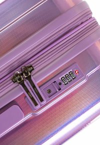 Maleta rígida morada con una superficie texturizada, doble cremallera y un candado aprobado por la TSA. Presenta un disco de combinación en la parte frontal.