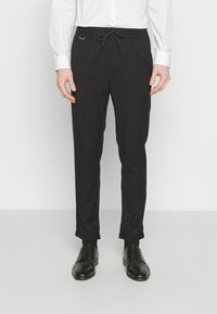 Pantalons noirs cintrés avec une taille à cordon, dotés d'une texture de tissu lisse et de poignets roulés, associés à des chaussures de ville noires.