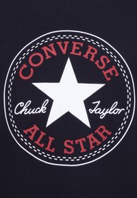 Black t-shirt featuring a round graphic with a white star, red text saying "CONVERSE" and "ALL STAR," and "Chuck Taylor" in white script lettering.