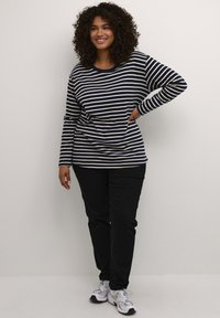 Navy and white striped long-sleeve shirt with a round neckline, paired with black pants and white athletic shoes.
