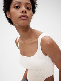 Hedvábný, světle krémový crop top s širokými ramínky a čtvercovým výstřihem. Hladká textura a těsně přiléhající střih zvýrazňují kontury těla.