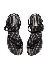 Schwarze Flip-Flops mit glänzenden Riemen und einem gemusterten Fußbett, das wellenförmige schwarze und graue Designs sowie weiße Akzente aufweist. Schnallen-Detail am Riemen.