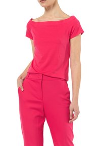 Fuksjowa bluzka na jedno ramię z krótkimi rękawami, gładka bawełniana tkanina, luźny fason, w połączeniu z dopasowanymi spodniami wąskimi.