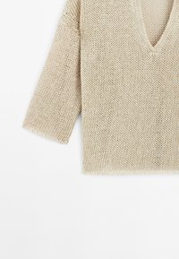 Beige gebreide pullover met een brede V-hals, drop shoulder mouwen en een losse pasvorm. Gestructureerde stof met een open weefpatroon.