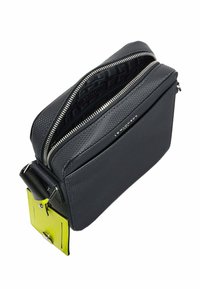Borsa in pelle nera con texture, dotata di due scomparti con zip e un tag giallo. Presenta una forma strutturata e una tracolla removibile.