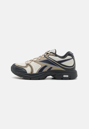 Scarpe da ginnastica beige e bianche con dettagli neri, pannelli in rete testurizzata e suola ammortizzata. Presentano elementi di design viola e lacci.
