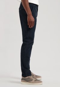 Mornarsko plave slim-fit hlače od mekog materijala, s prednjim gumbom, upotpunjene svijetlosivim i krem tenisicama.