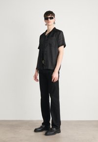 Camicetta corta a righe nere con bottoni, abbinata a pantaloni neri a gamba dritta e scarpe nere chunky. Gli accessori includono occhiali da sole.