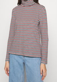 Gestreifter Rollkragenpullover in Weiß, Rot und Schwarz, aus weichem Stoff. Lange Ärmel mit lockerer Passform und geradem Saum am Ende.