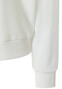 Nahaufnahme von einem weißen gerippten Bündchen und Saum eines langärmligen Sweatshirts mit weichem, glattem Stoff.